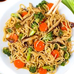 a white plate topped with noodles, carrots and broccoli next to celery