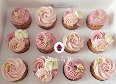 cupcakes with pink frosting and gold decorations in a white box on top of a table