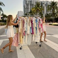 two women are trying to sell clothes on a rack in front of palm trees and high rise buildings