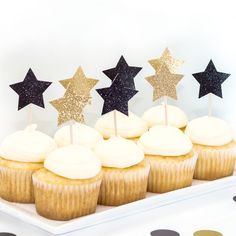 cupcakes with white frosting and gold stars on top sit on a plate