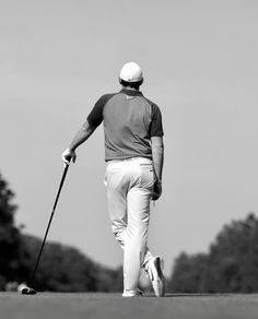 black and white photograph of a man walking with a golf club in his left hand