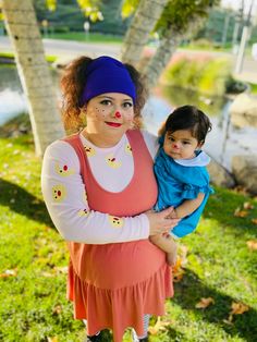 a woman holding a baby in her arms while standing next to a tree and water