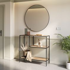 a round mirror hangs on the wall above a shelf with books, plants and vases