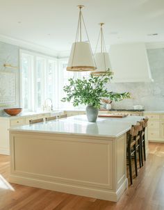 a large kitchen with an island in the middle and two hanging lights above it, along with bar stools