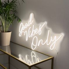 a neon sign that says good vibes only on it next to a potted plant