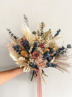 a bouquet of dried flowers is held up by someone's hand against a white wall