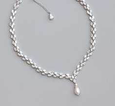 a white necklace with pearls on it and a diamond droplet hanging from the side