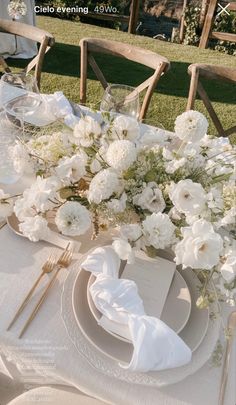 the table is set with white flowers and place settings