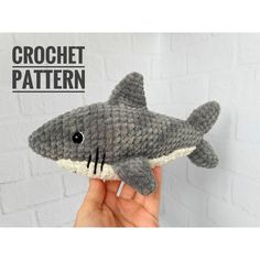 a hand holding a stuffed shark toy in front of a white brick wall with the words crochet pattern on it