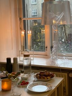 the table is set with food and candles in front of an open window that looks out onto a city street