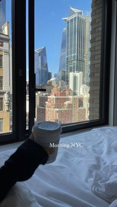 a person's hand holding a coffee cup in front of a window overlooking the city