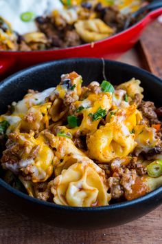 two black bowls filled with pasta and meat on top of a wooden table next to another bowl