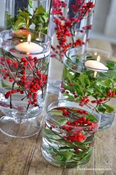 three glass vases filled with red berries and greenery on top of a wooden table