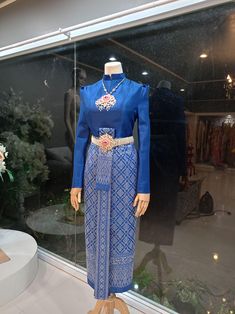 a mannequin wearing a blue dress in front of a window with flowers on display