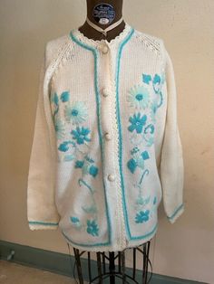 a white cardigan with blue flowers on it sitting on a mannequin stand