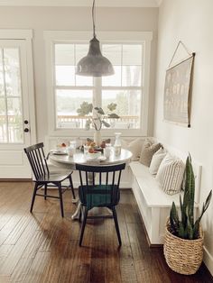 a dining room table with chairs and a bench in front of the window next to a potted plant