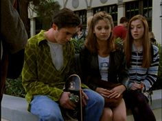 three young people sitting on a bench with one holding a skateboard and the other looking at his cell phone