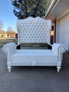 a white couch sitting on top of a sidewalk next to a garage door in front of a house