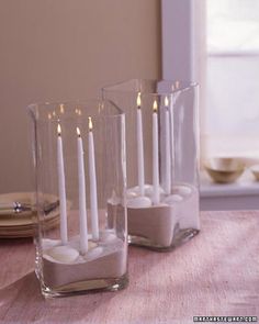 there are many candles that are in the glass vases on the table with sand