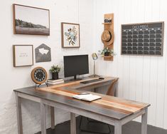 a wooden desk topped with a computer monitor next to a clock and wall mounted pictures