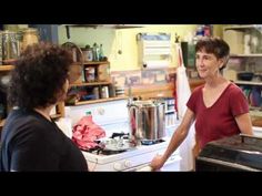 two women are talking in the kitchen while one woman is cooking something on the stove