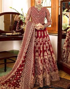 a woman standing in front of a mirror wearing a red and gold bridal gown