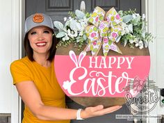 a woman holding up a sign that says happy easter in front of a door with flowers