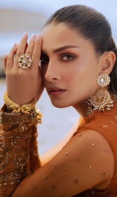 a woman in an orange dress holding her hand up to her face and wearing gold jewelry