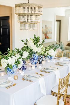 the table is set with blue and white dishes, gold place settings, and greenery