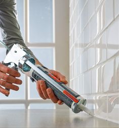 two hands are holding a drill in front of a white tile wall and window sill