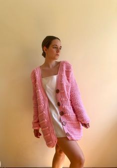 a woman standing in front of a wall wearing a pink cardigan and white dress