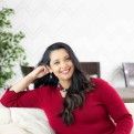 a woman sitting on a couch smiling at the camera with her hands behind her head