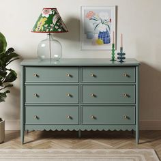 a green dresser sitting next to a lamp on top of a wooden floor