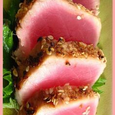 three slices of tuna with sesame seeds on top of lettuce and garnished with sesame seeds