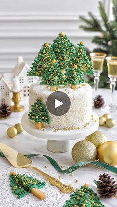 a christmas cake decorated with pine trees and gold baubles on a table surrounded by other holiday decorations