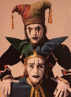 two clowns dressed in costumes and hats, one with his head turned to the side