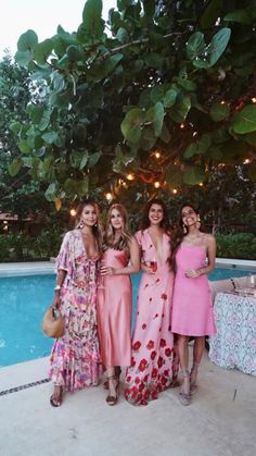 four women standing next to each other in front of a pool with lights strung overhead