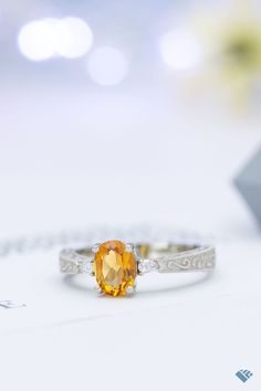 a close up of a ring with an orange stone in it on a white surface