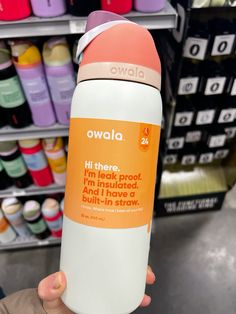 a person holding up an orange and white bottle in front of shelves with other items