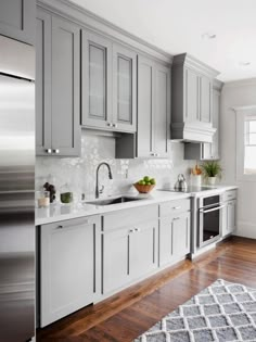 a kitchen with gray cabinets and white counter tops, hardwood floors, and a rug on the floor