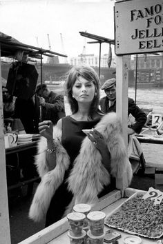 black and white photograph of woman in fur coat sitting on boat with other people around her