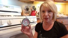 a woman standing in front of an oven holding a thermometer