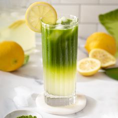 a tall glass filled with green liquid next to lemons