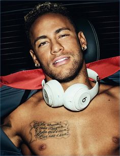 a shirtless man with headphones on is looking at the camera and has tattoos on his chest