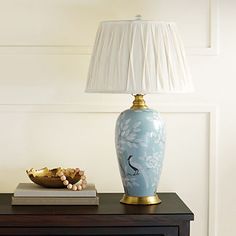 a blue vase sitting on top of a wooden table next to a lamp and bowl