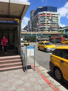 there is a woman that is standing at the entrance to a building with taxi cabs parked in front of it