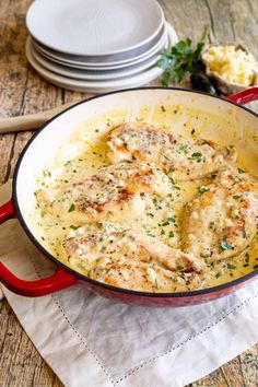 a red skillet filled with chicken and gravy on top of a wooden table