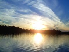 the sun is setting over a lake with trees in the background and clouds in the sky