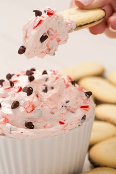 a person holding a cracker over a cupcake with white frosting and sprinkles