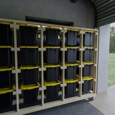 several black and yellow bins are lined up in a storage area with shelves on each side